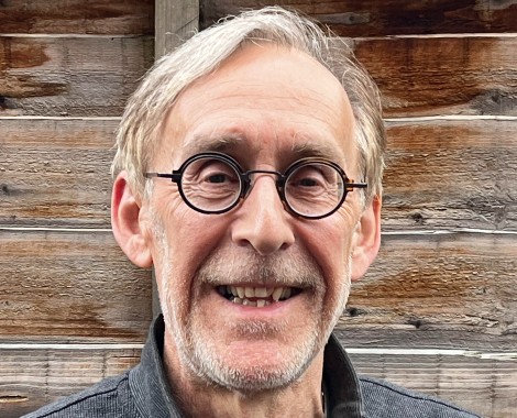 A headshot of a Caucasian male wearing glasses in front of a wooden panel fence.